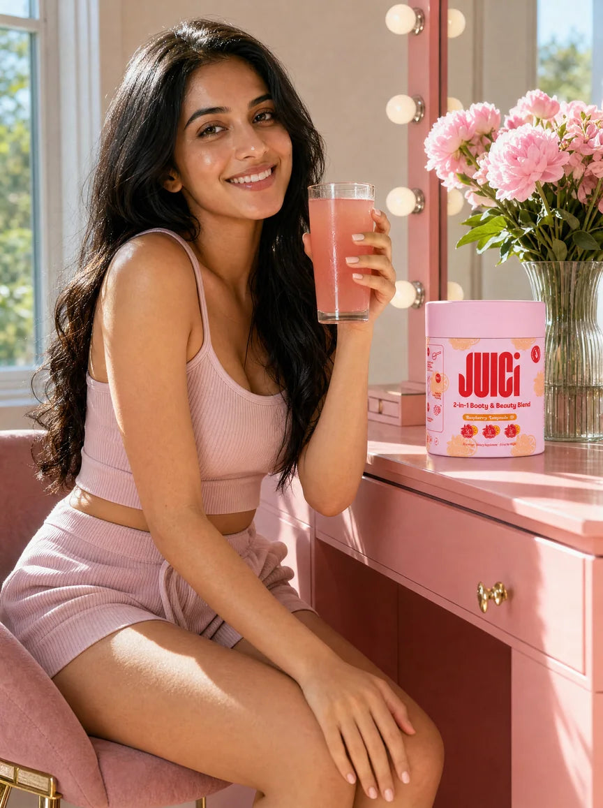 Woman in a blush lounge set at her pink dressing table with a glass of JUICi and a tub of JUICi Raspberry Lemonade